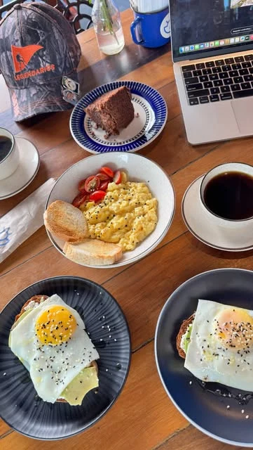 Mesa de café da manhã com ovos, torradas, café e um notebook.
