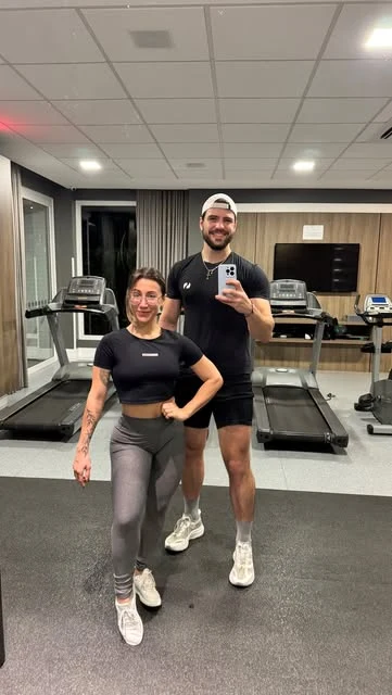 Mariana e um parceiro registrando um treino diante do espelho na academia.